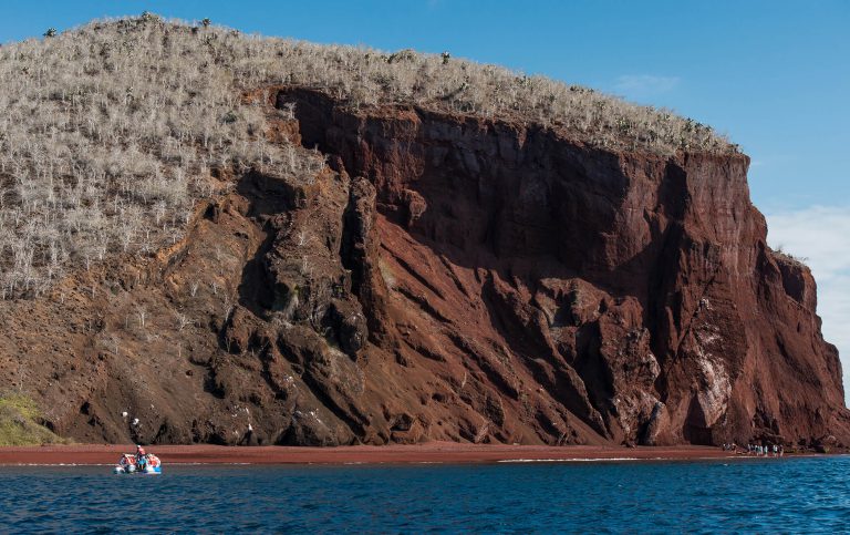 Rabida in Galapagos Islands, view of the red sand and hill with tourist wallking near to the boat