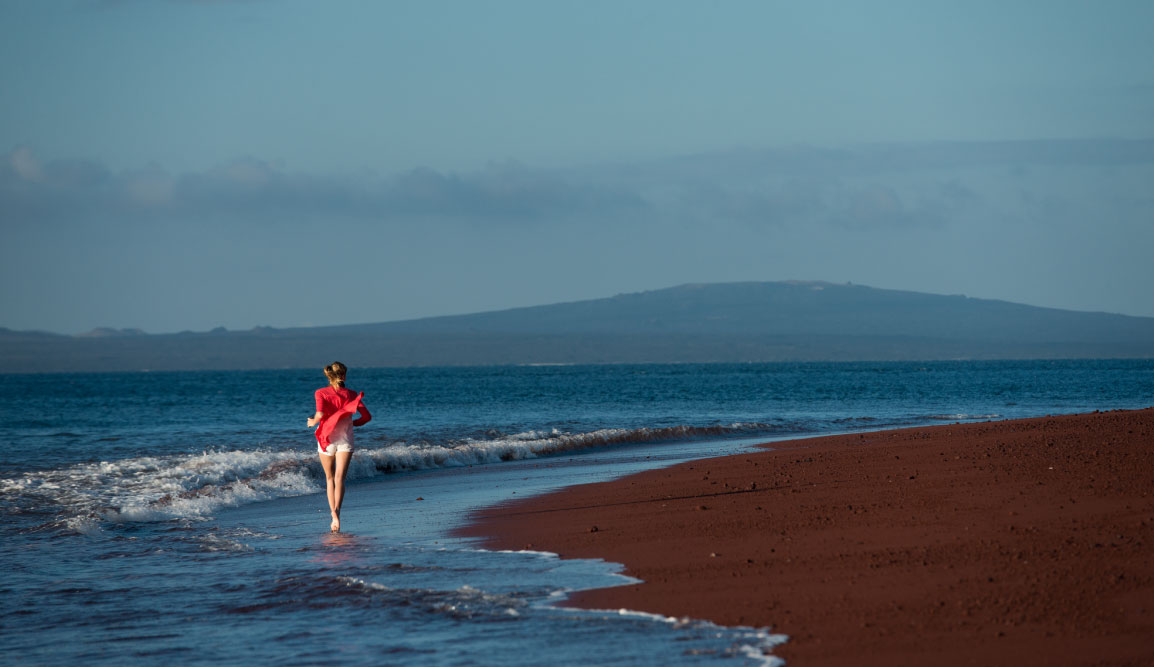 Rabida in Galapagos Islands with a red sand beach and a tourist girl jogging